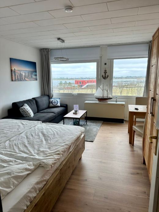 Wohn- und Schlafraum mit Doppelbett, Sofa und Blick zum Yachthafen
